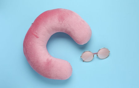 Pink travel pillow and sunglasses on light blue background, flat layの写真素材
