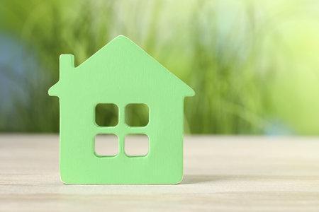 Mortgage concept. House model on white wooden table against blurred green background, space for textの写真素材