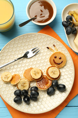 Creative serving for kids. Plate with cute caterpillar made of pancakes, grapes and banana on light blue wooden table, flat layの写真素材
