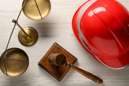 Law concept. Gavel, scales and red hard hat on white wooden table, flat layの写真素材