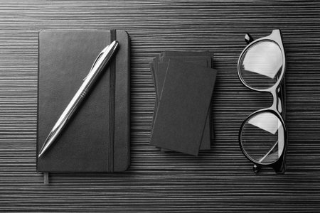 Blank black business cards, glasses and stationery on wooden table, flat lay. Mockup for design