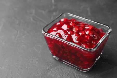 Fresh cranberry sauce in glass bowl on gray textured table, closeup. Space for textの写真素材