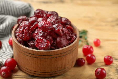 Tasty dried cranberries in bowl and fresh ones on wooden table, closeupの写真素材