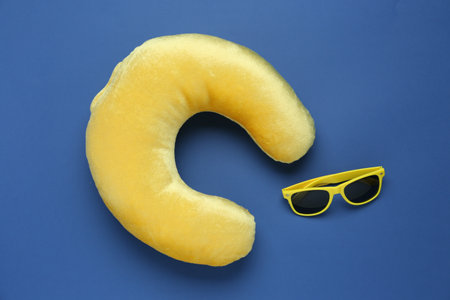 Yellow travel pillow and sunglasses on blue background, flat lay