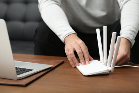 Man inserting cable into Wi-Fi router at wooden table indoors, closeupの写真素材