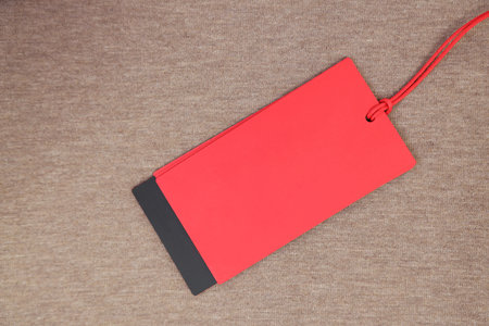 Red tag on brown garment, top view. Space for text