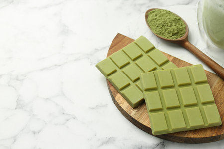 Pieces of tasty matcha chocolate bar and powder in spoon on white marble table, closeup. Space for textの写真素材