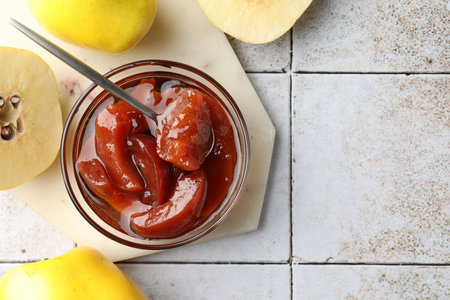 Tasty homemade quince jam in bowl, spoon and fruits on tiled table, flat lay. Space for textの写真素材