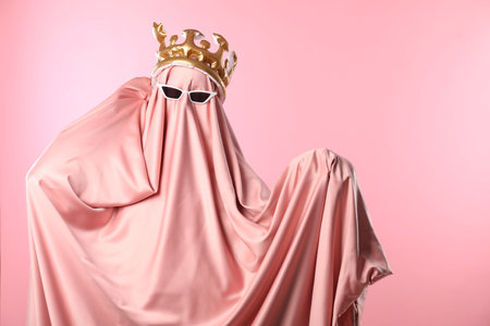 Glamorous ghost. Woman in sheet with sunglasses and crown on pink background, space for textの写真素材