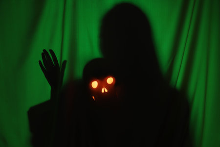 Silhouette of creepy ghost with skull behind dark green cloth