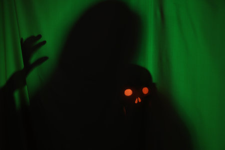 Silhouette of creepy ghost with skull behind dark green clothの写真素材