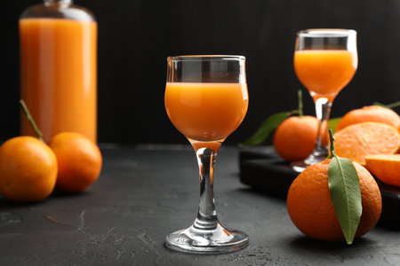 Tasty tangerine liqueur and fresh fruits on black textured tableの写真素材