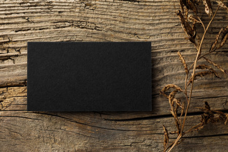 Empty black business card and dried plant on wooden background, top view. Mockup for designの写真素材