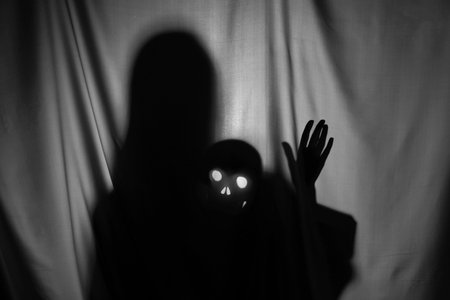 Silhouette of creepy ghost with skull behind gray clothの写真素材