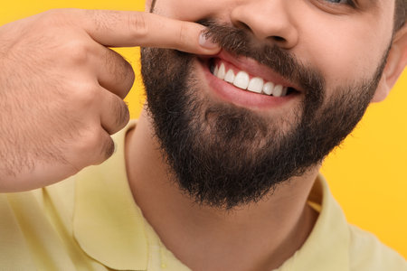 Man showing his clean teeth on yellow background, closeup