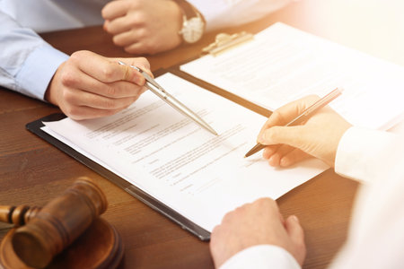 Lawyer pointing at document and client putting signature at wooden table in office, closeupの写真素材