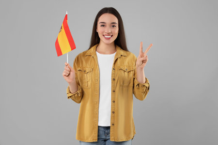 Young woman holding flag of Spain on light gray backgroundの写真素材