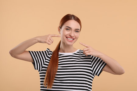 Beautiful woman showing her clean teeth and smiling on beige backgroundの写真素材