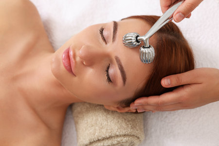 Young woman receiving facial massage with metal roller in beauty salon, above viewの写真素材
