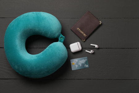 Turquoise travel pillow, passport, credit card and earphones on black wooden background, flat lay. Space for textの写真素材