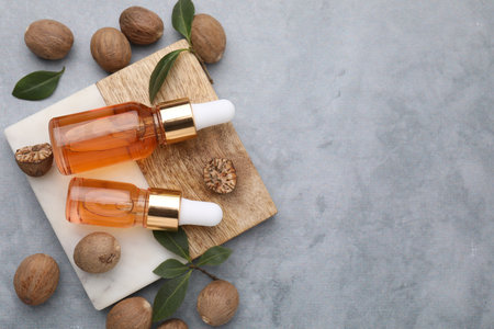Nutmeg essential oil, nuts and leaves on light gray table, flat lay. Space for textの写真素材