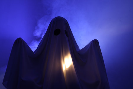 Creepy ghost. Woman covered with sheet in blue lightの写真素材