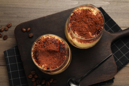 Delicious tiramisu in glasses, spoon and coffee beans on wooden table, top viewの写真素材