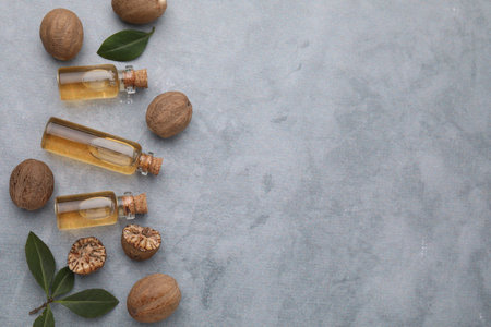 Nutmeg essential oil, nuts and leaves on light gray table, flat lay. Space for textの写真素材