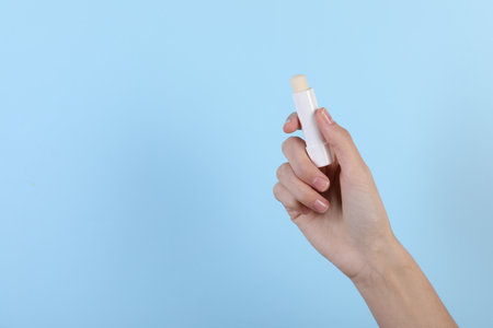 Woman with lip balm on light blue background, closeup. Space for text