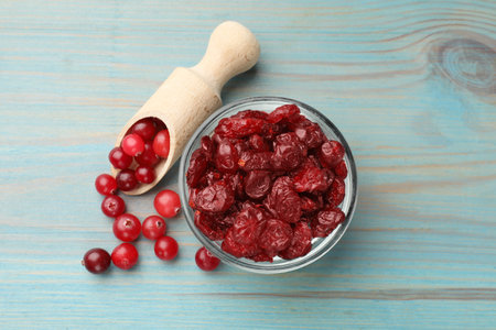 Tasty dried cranberries in bowl and fresh ones on light blue wooden table, top viewの写真素材