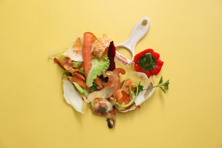 Peels of fresh vegetables and peeler on yellow background, flat layの写真素材