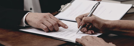 Lawyer pointing at document and client putting signature at wooden table in office, closeup. Banner...