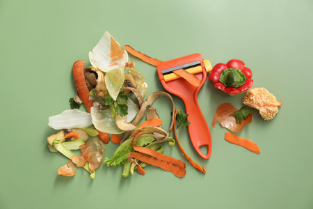 Peels of fresh vegetables and peeler on green background, flat layの写真素材