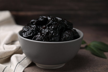 Sweet dried prunes in bowl on brown table, closeupの写真素材