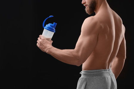 Young man with muscular body holding shaker of protein on black background, closeupの写真素材