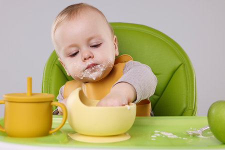 Cute little baby eating healthy food in high chair on gray backgroundの写真素材