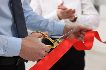 Man cutting red ribbon with scissors on blurred background, closeupの写真素材