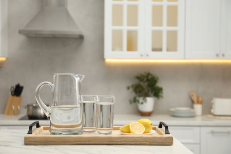 Jug, glasses with clear water and lemons on white table in kitchen, space for textの写真素材