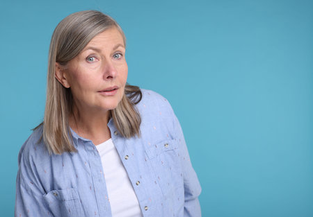 Portrait of surprised senior woman on light blue background, space for text