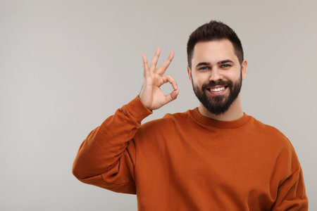 Man with clean teeth showing OK gesture on gray background, space for textの写真素材