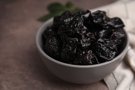 Sweet dried prunes in bowl on brown table, closeup. Space for textの写真素材