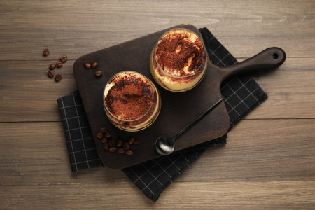Delicious tiramisu in glasses, spoon and coffee beans on wooden table, top viewの写真素材