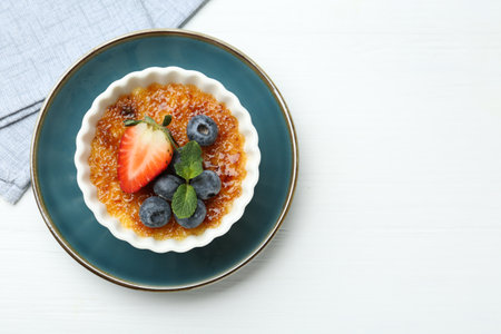 Delicious creme brulee with berries and mint in bowl on white wooden table, top view. Space for textの写真素材