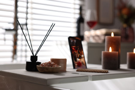White wooden tray with aroma diffuser, beauty products and burning candles on bath tub in bathroomの写真素材
