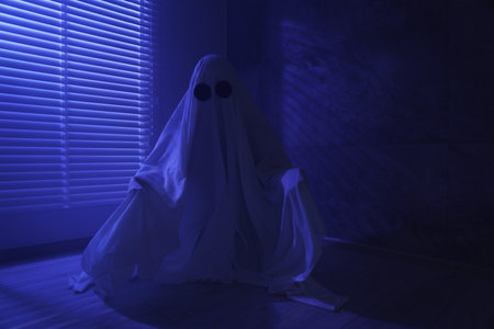 Creepy ghost. Woman covered with sheet near window in blue light