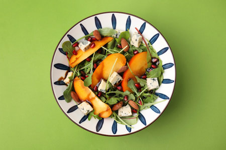 Tasty salad with persimmon, blue cheese, pomegranate and almonds served on light green background, top viewの写真素材