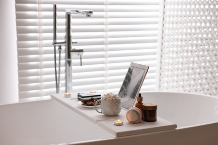 White wooden tray with tablet, spa products, hot drink and burning candle on bathtub in bathroomの写真素材