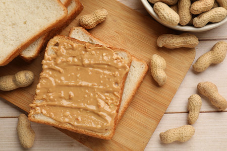 Delicious toasts with peanut butter and nuts on light wooden table, flat lay