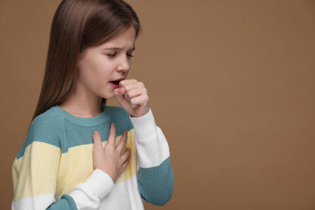 Sick girl coughing on brown background, space for text