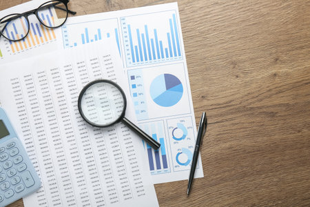 Accounting documents, magnifying glass, stationery and glasses on wooden table, top view. Space for...